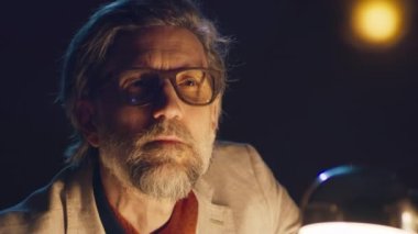 Gözlüklü konsantre tiyatro yönetmeni, karanlık bir salonda, elinde lambayla oturup gelecek bir performansın provasını izliyor.