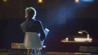 Yönetmen gösteri provasından sonra tiyatronun sahnesinde bir sandalyede otururken dinleniyor ve senaryoyu elinde tutarak ayrılıyor.