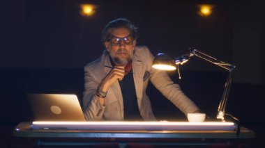 Yönetmen, karanlık bir tiyatroda lambayla aydınlatılmış bir masada otururken performansın provasını izliyor ve senaryoda notlar alıyor.