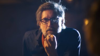 A professional director in glasses together with the theatrical cast talking about the details of the script, for the performance sitting on a dim stage