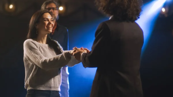 An actress and an actor rehearsing a love scene on a theater stage with a spotlight while a male director watching them