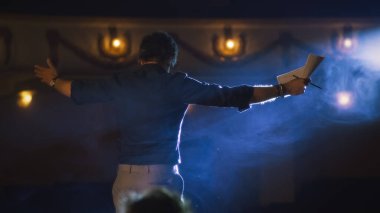 Oyuncular, oyunun provası sırasında sahnede dumanlı ve spot ışıklarıyla rol yapma konusunda ciddi bir yönetmenin talimatlarını dinliyorlardı.