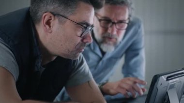 Gözlüklü bir adam, dijital tablet bilgisayardan araklarken araba kontrolü ve onarım konularında erkek bir müşteriye danışıyor.