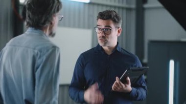 Cheerful car service manager in repair shop with tablet and client shaking hands after successfully diagnosing and repairing car