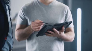 Crop view of mechanic service manager in repair shop weared t-shirt consulting a client in a car service, using tablet and discussing the results of a car checking and diagnostics