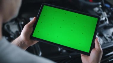 Tanımlanamayan erkek araba servisi çalışanı, açık kaputun yanında dururken yeşil ekran kromatonlu dijital tablet bilgisayar kullanarak arabayı kontrol ediyor ve bakım yapıyor.