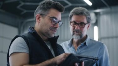 Bir araba servisinde müşteriyle konuşurken dijital tablet bilgisayardan araklayan tamirci bir arızanın ardından bir arabanın teşhisi hakkında konuşuyor.