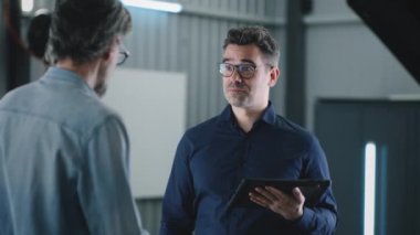 Manager in a suit with a tablet shaking hands with a male client after car diagnostics in a car service, and looking at the camera