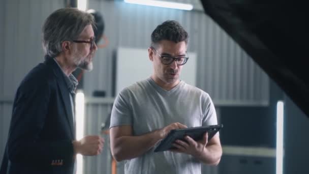 Ein Mechaniker Mit Brille Und Tablet Steht Neben Einem Kunden — Stockvideo