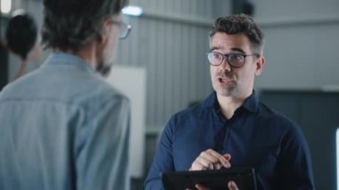 Car service manager in glasses consulting a client on car diagnostics and breakdown repair using a modern tablet
