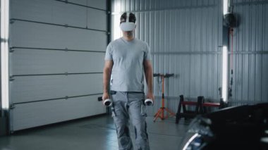 Man worker in uniform in a modern virtual reality glasses with controllers checking and testing a car after repairing in a car service