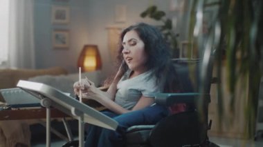 Happy female painter with disability in a wheelchair smiling and looking at the camera while painting at home