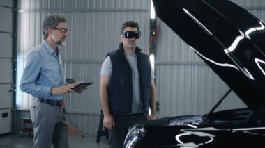 Manager in a suit and a mechanic in a virtual reality headset talking and standing near the car during the diagnostics, and maintenance in a car service