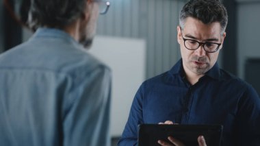 Araba servisi yöneticisi modern bir tablet kullanarak bir müşteriye araba kontrolü ve arıza onarımı konusunda danışmanlık yapıyor.