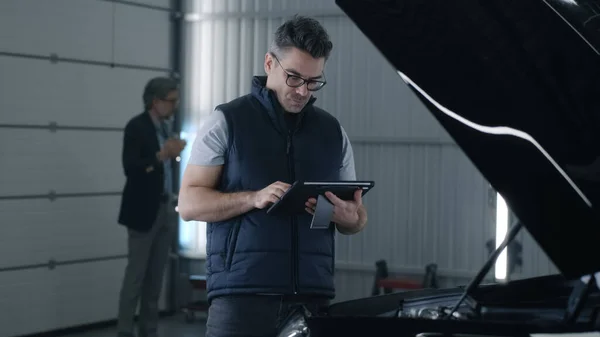 Mechanic Glasses Swiping Tablet While Standing Bonnet Checking Results Car — Zdjęcie stockowe