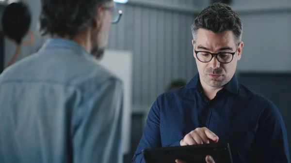 Manager in casual clothes with a tablet talking to a male client in a car service and discussing checking and diagnosing a car