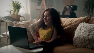 Woman with spinal muscular atrophy sitting on a sofa at home smiling and communicating using laptop while having video call