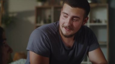 A male caregiver sitting on a couch in living room next to a woman with a physical disability and communicating with her