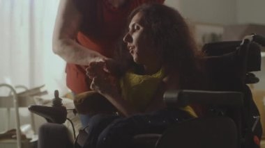 Elderly woman taking care and helping her daughter with a disability while she sitting in a modern electric wheelchair and then leaving the room
