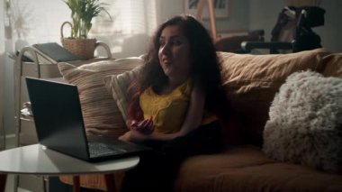 Woman with disability talking via video call with friend using laptop while sitting on a couch in cozy living room in her spare time