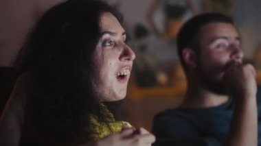 Woman with a disability and man rejoicing and discussing movie while watching it on TV together at home in the evening