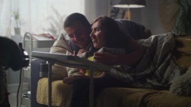 Man hugging his wife with a disability who sitting on a sofa and they talking and discussing drawing on digital tablet computer, together at home