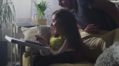 Woman with a disability drawing on digital tablet computer using pencil and talking with husband, while sitting on a couch at the table at home