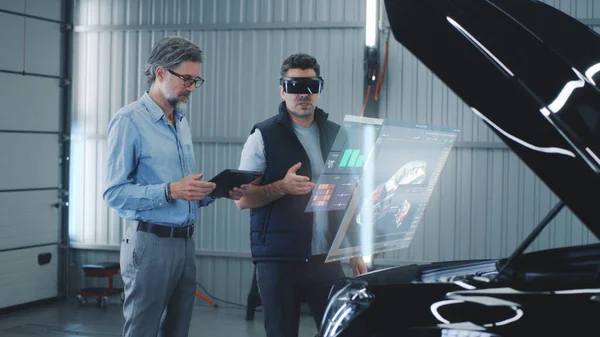 Two specialists carry out car diagnostics using modern tools. They study the indicators and graphs on the screen, displaying the condition of the car. Carrying out repairs in a technological workshop.