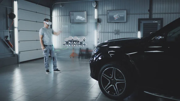 Car service manager assembling a car engine in a futuristic virtual reality program using a joystick and a virtual reality helmet