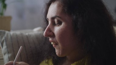 Woman with a physical disability using application for drawing illustrations with pen on a digital tablet computer sitting at home on a sofa