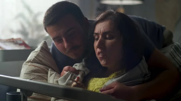 Woman with a disability sitting on a couch at the table, using digital tablet computer and pencil while her husband entering the room and covering her with a blanket