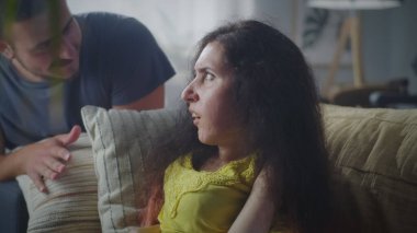 Confused woman with a disability sitting on a couch and talking with nervous man while they arguing and having quarrel