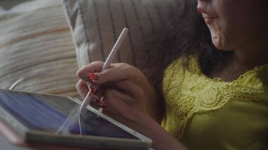 Woman with a disability smiling while drawing on digital tablet computer with stylus sitting on a couch at home