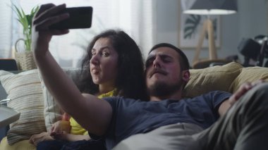 Woman with a physical disability and man laughing and taking a selfie together on smartphone for social networks sitting on a couch at home