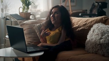 Woman with disability talking via video call with friend using laptop while sitting on a couch in cozy living room in her spare time