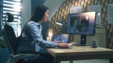 3 boyutlu elektro gitar ve grafik yapan Asyalı kadın tasarımcı, evde bilgisayar ve tablet üzerinde çalışırken 3D projeleri modellemek için yazılım kullanıyor..