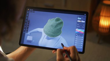 Genç erkek 3D tasarımcı dijital tablet bilgisayar ve stylus kullanarak tasarım uygulamasında kıyafetlerin 3D görselleştirilmesi üzerinde çalışıyor.