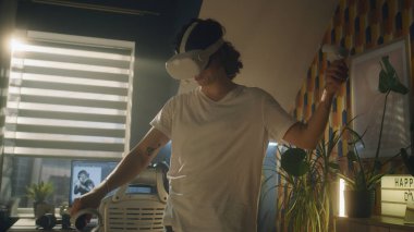 Adam evde video oyunu oynarken boş zamanlarında VR kulaklık ve kablosuz kumanda kullanıyor. Sanal gerçeklik cihazı. Siber uzay ve metaevren