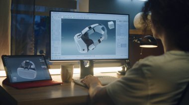 Evden çalışan ve bilgisayar ve dijital tablet kullanarak profesyonel 3D modelleme yazılımında modern VR gözlüklerinin 3 boyutlu prototipini yapan genç bir erkek.