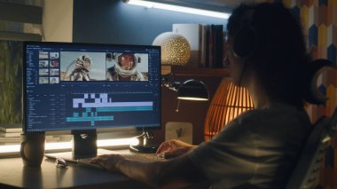 Profesyonel programda astronotlarla video montajı yapan kulaklıklı adam evde bilgisayar başında çalışıyor.