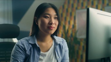 Asyalı kadın ev ofisinin masasında oturuyor ve kişisel bilgisayarda uzaktan çalışıyor ya da boş zamanlarında internette geziniyor.