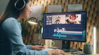 Kulaklıklı Asyalı kadın ev ofisinden bilgisayar üzerinde çalışıyor ve profesyonel programdaki müşteriler için astronotlarla video düzenliyor.