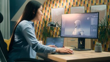 Asyalı bir kadın ev ofisinde çalışırken bilgisayar ve dijital tablet kullanarak profesyonel programda video oyunu karakterinin 3 boyutlu modelini oluşturuyor.