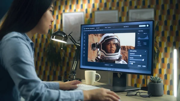 Female asian freelancer editing picture with astronaut on computer in photo editing software while working remotely from home office