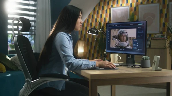 Female asian freelancer editing picture with astronaut on computer in photo editing software while working remotely from home office