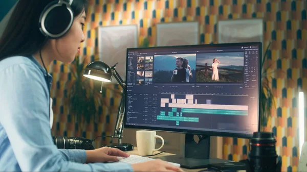 Concentrated asian woman sitting at the table and editing video for client in professional software using modern computer while working at home