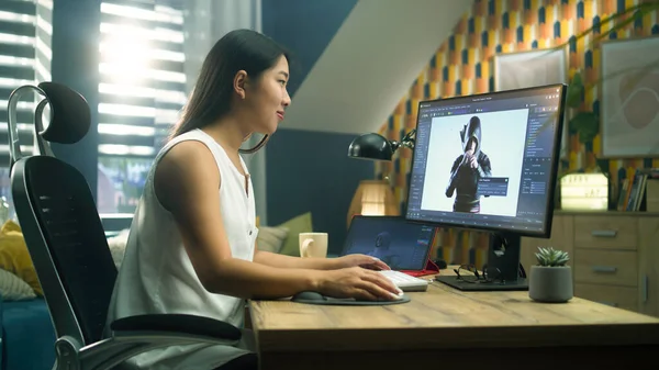 Asian woman creating 3D model of video game character in professional program using computer and digital tablet while working at home office