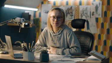 Ev tasarımı bir stüdyoda yaratıcı tasarımcı eskiz yapmayı bırakır ve gülümseyen kameraya bakar. Kalem taslakları, çizim tahtası, video düzenleme, hikaye anlatma.