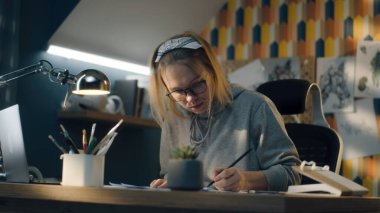 Yaratıcı tasarımcı kısa bir aradan sonra çizimleri üzerinde çalışmaya başlar. Gözlüklerini takar ve laptopunu açar. Kalem çizimi. Storyboard, video düzenleme, derleme, yaratıcı çalışma konsepti.