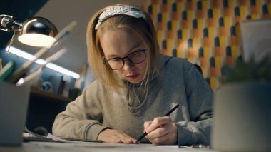 Odaklanmış illüstratör projesi için çizimler çiziyor. Gri kapüşonlu gözlüklü genç bayan sanatçı çalışma masasında oturuyor. Kalem çizimleri yapıyor. Hikaye anlatma konsepti.